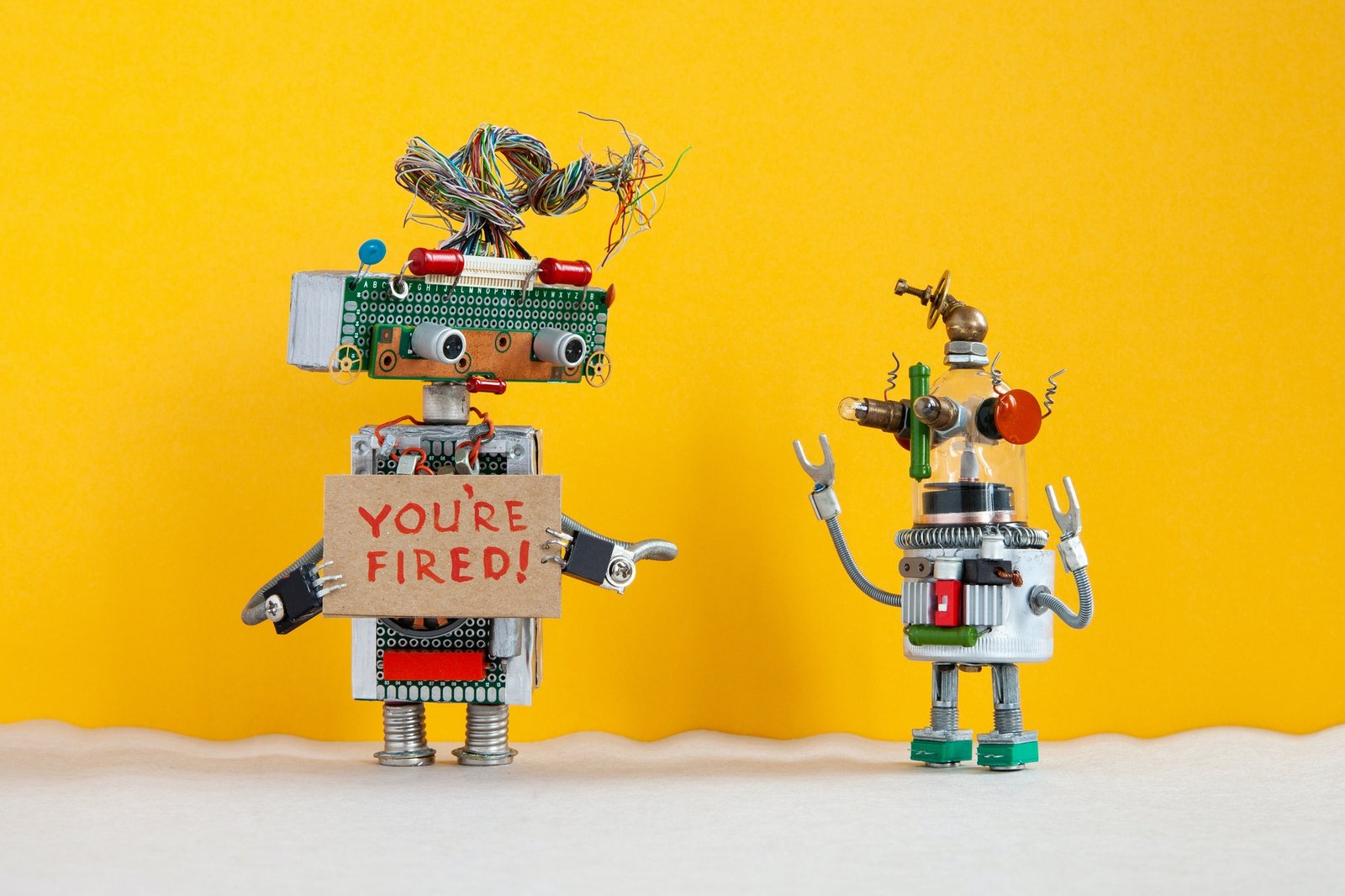 Robot chief dismisses younger robotic employer. Robotic character with a cardboard sign and|